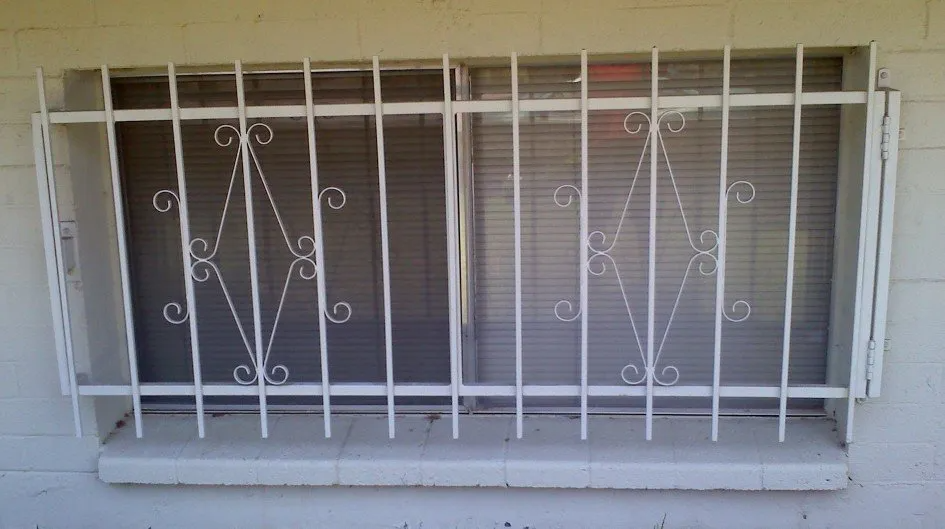 White security bars on a window. The bars have decorative diamond-shaped accents against a light-colored brick wall.