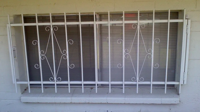 White barred window with decorative diamond pattern over a brick wall.