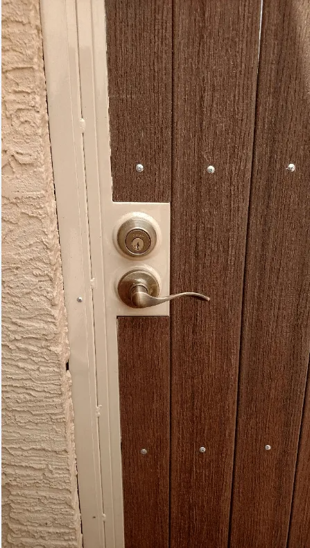 A brown wooden door with a white trim, a silver doorknob, and a deadbolt.