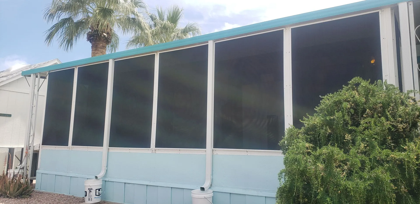 Light blue mobile home with black screens. Palm trees in background.