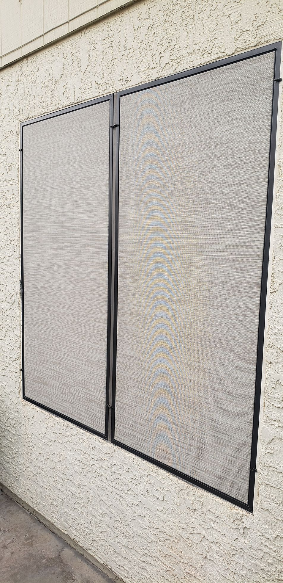 Two rectangular, gray screens on a stucco wall, connected by a black vertical frame.