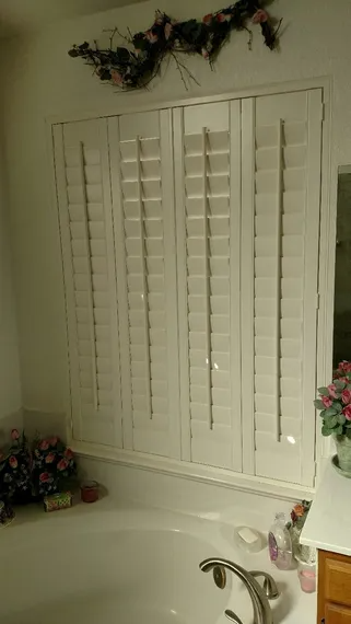 White shutters above a bathtub, with floral decor.