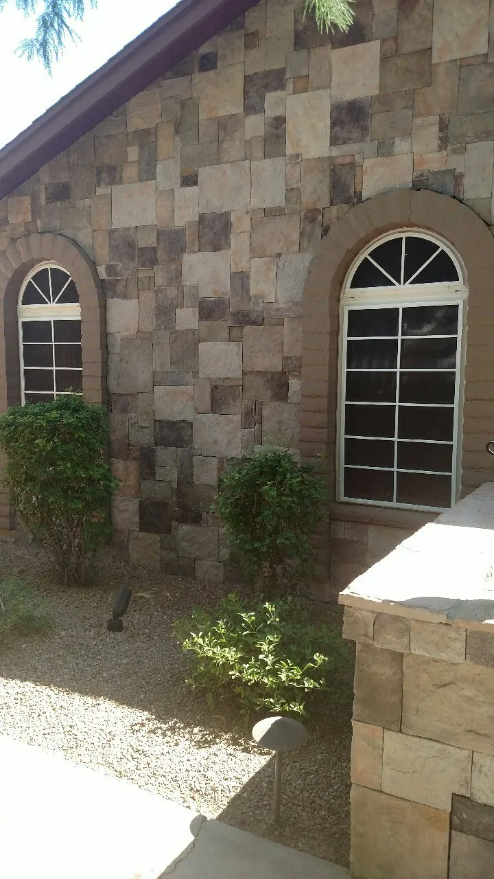 Stone building with arched windows and small bushes in front.