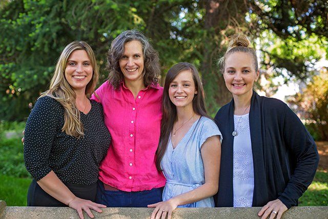 Four women are posing for a picture in front of a tree.