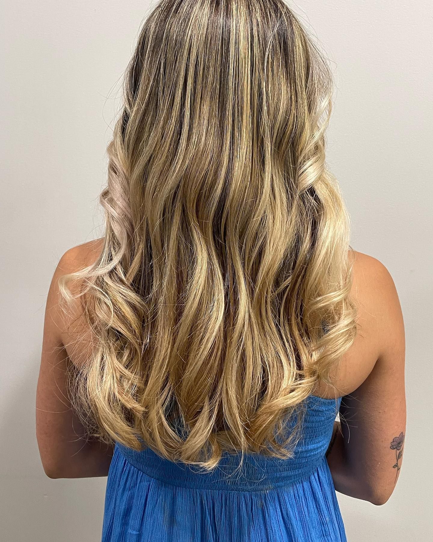 The back of a woman 's head with long blonde hair and a blue dress.