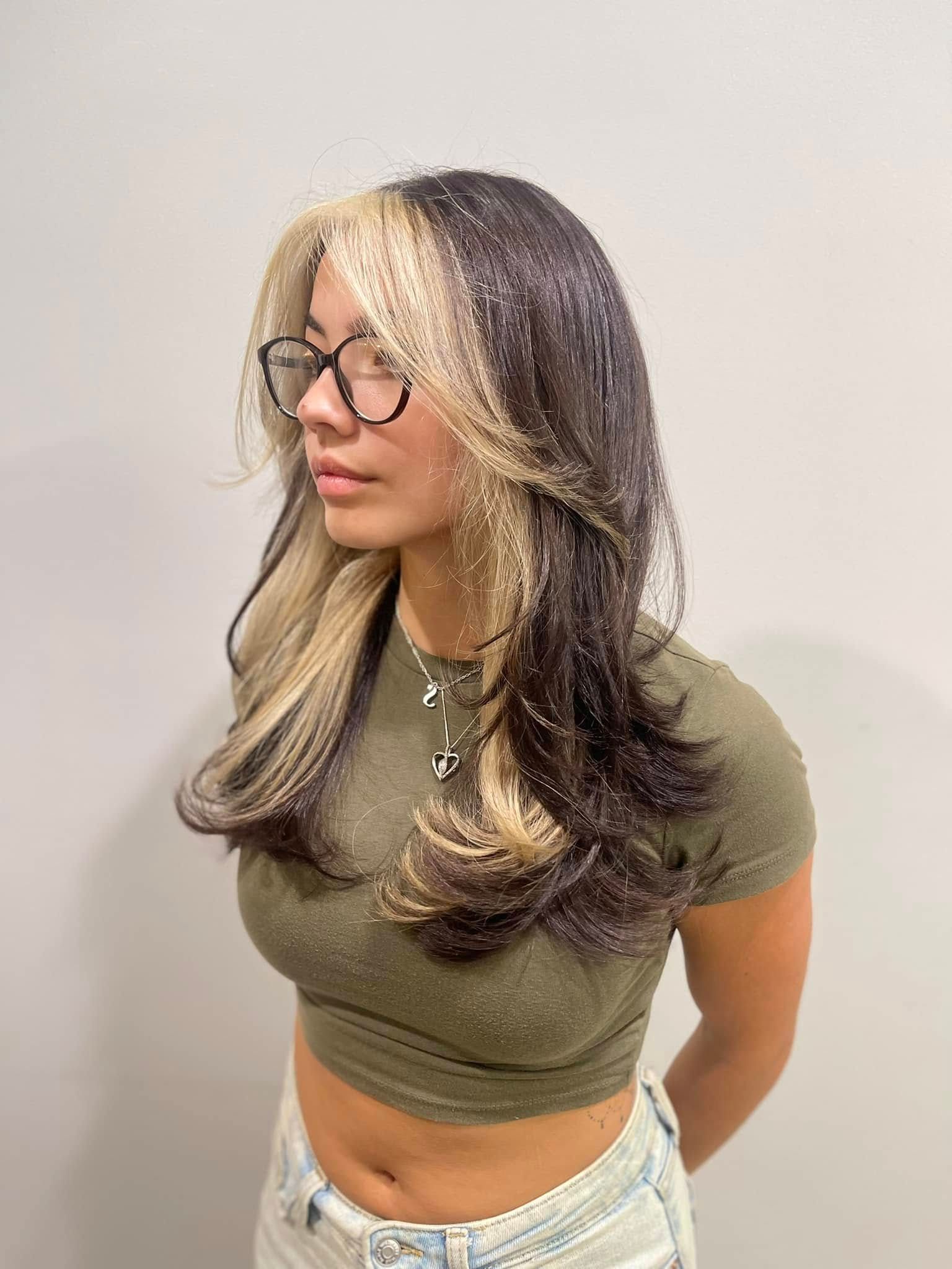 A woman with long hair and glasses is wearing a crop top and jeans.