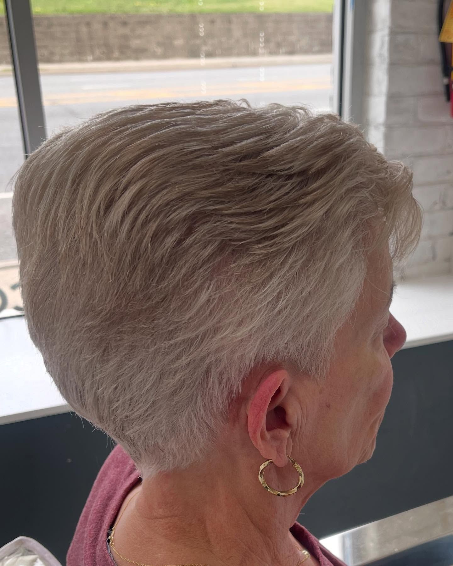 A woman with short gray hair is sitting in front of a window.