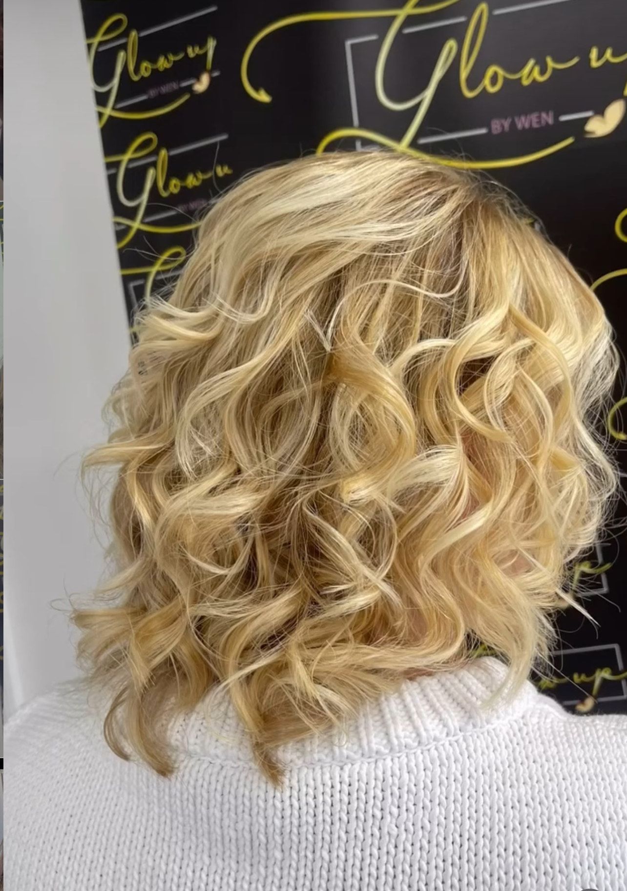A woman with blonde curly hair is wearing a white sweater.