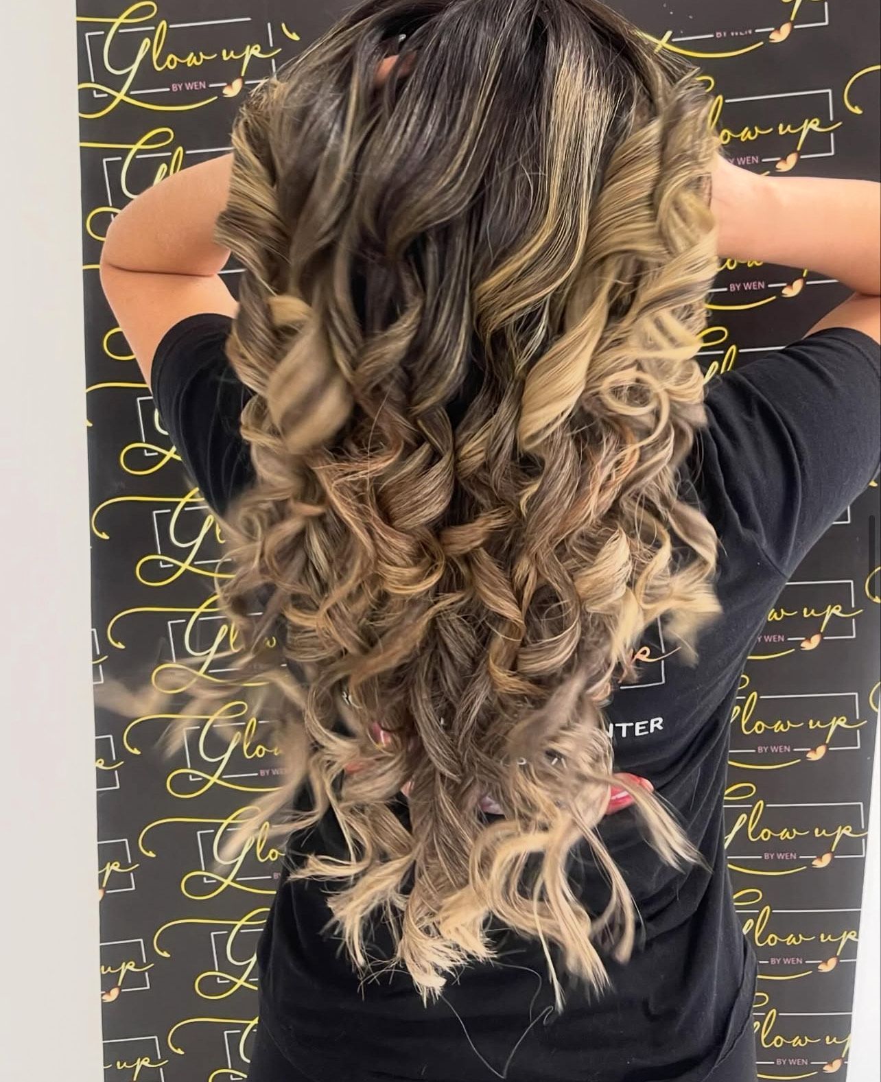 A woman with long curly hair is wearing a black shirt