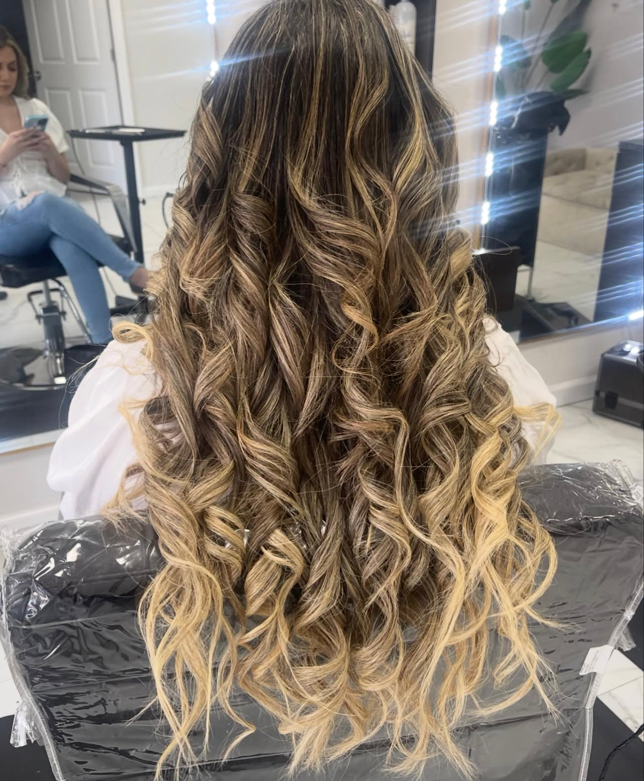 A woman with long curly hair is sitting in a chair in a salon.