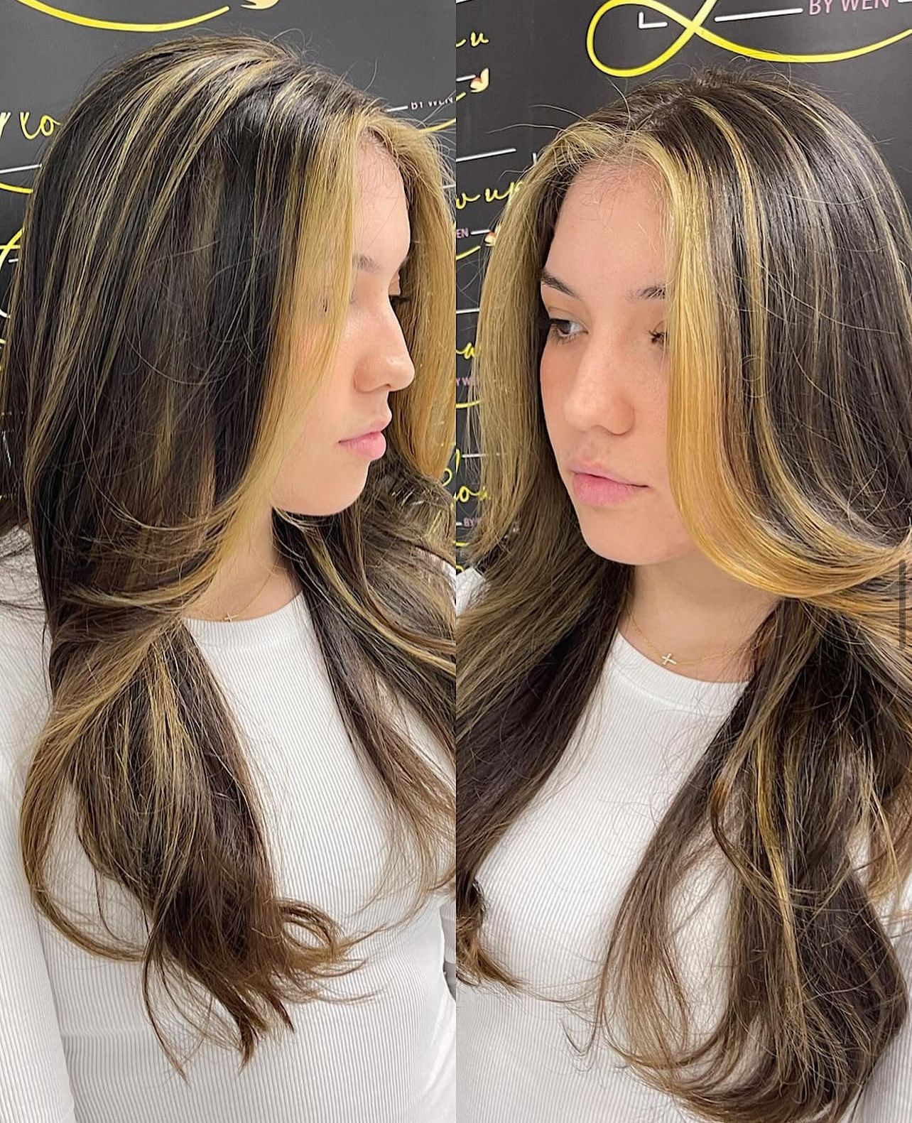 A woman with long brown hair and blonde highlights is wearing a white shirt.