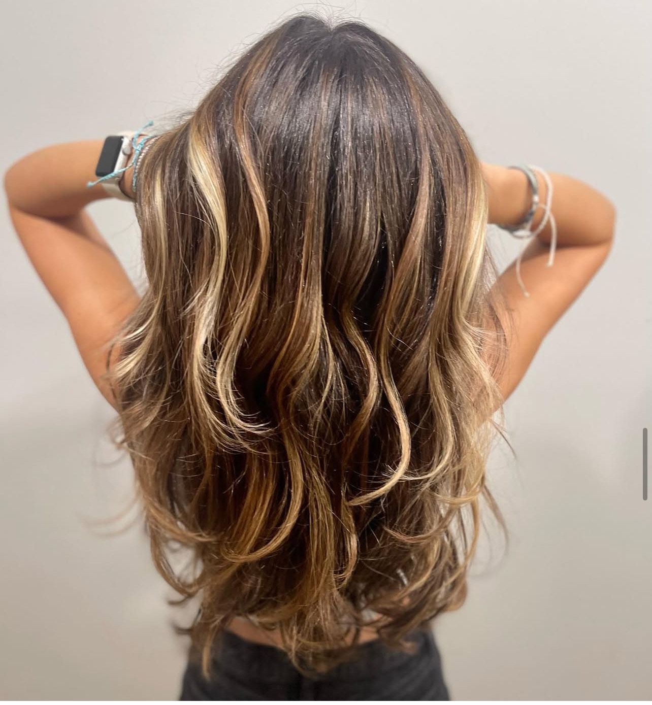A woman with long brown hair has her hands behind her head