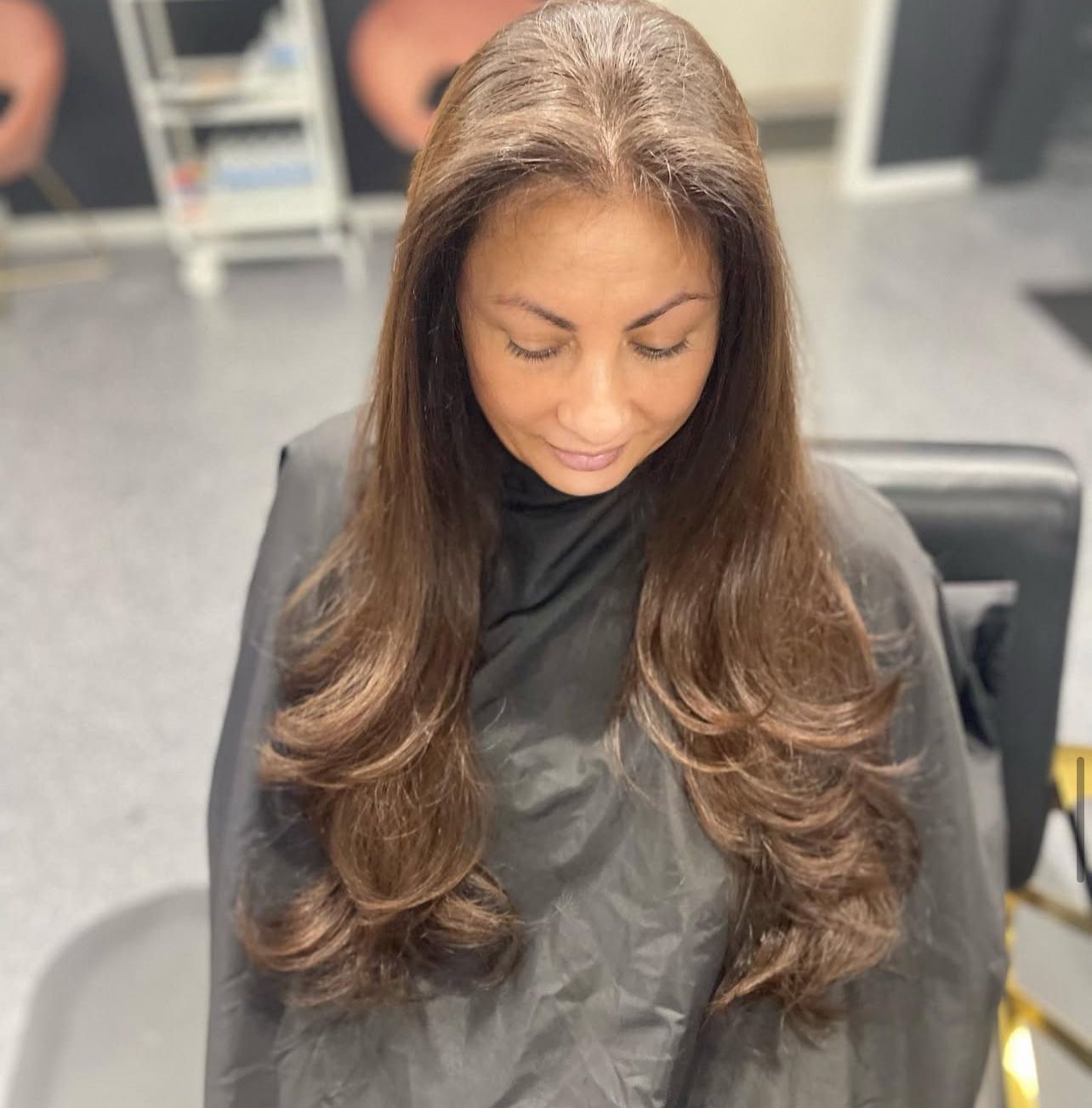 A woman with long brown hair is sitting in a chair wearing a black cape.