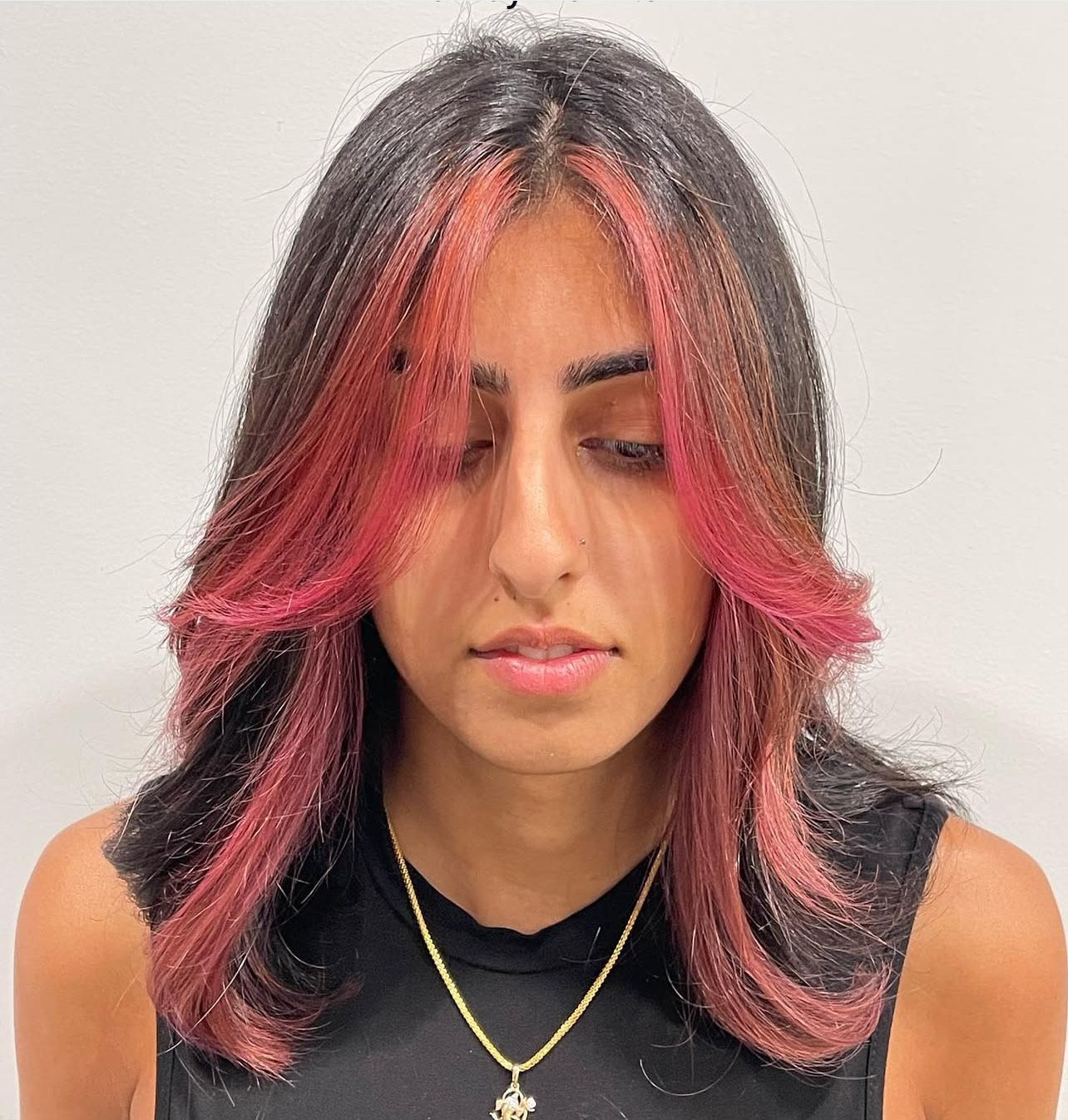 A woman with red hair is wearing a black tank top and a gold necklace.