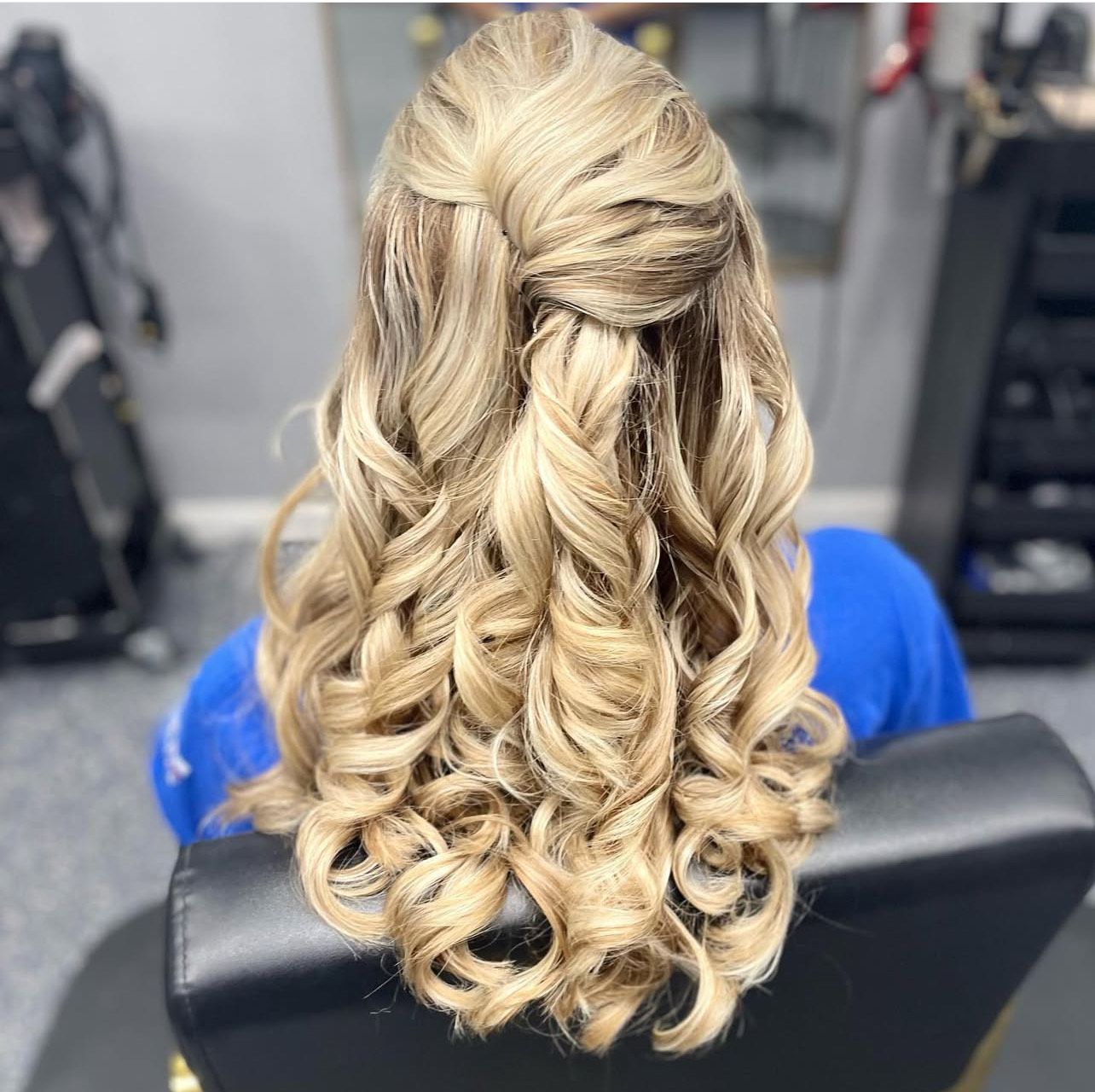 A woman is sitting in a chair with her hair in a half up half down hairstyle.