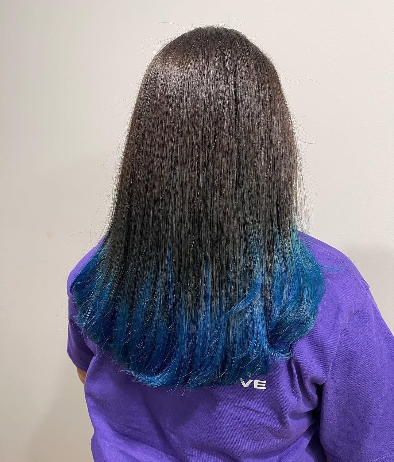 A woman with long black hair and blue highlights is wearing a purple shirt.