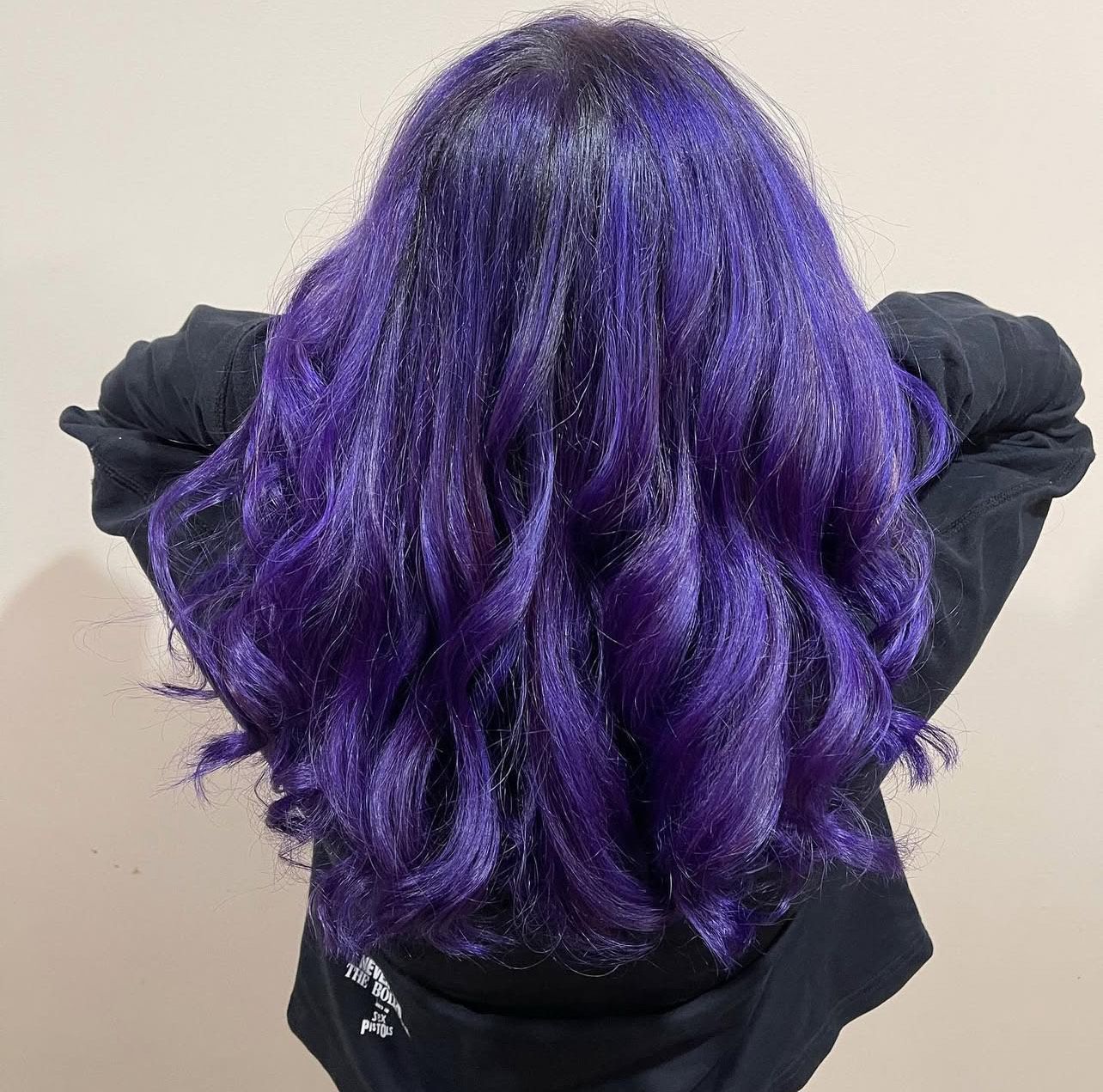 A woman with purple hair is wearing a black jacket.