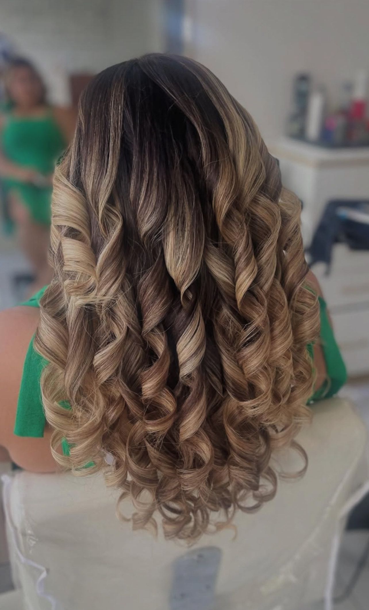 A woman with long curly hair is sitting in a chair in front of a mirror.