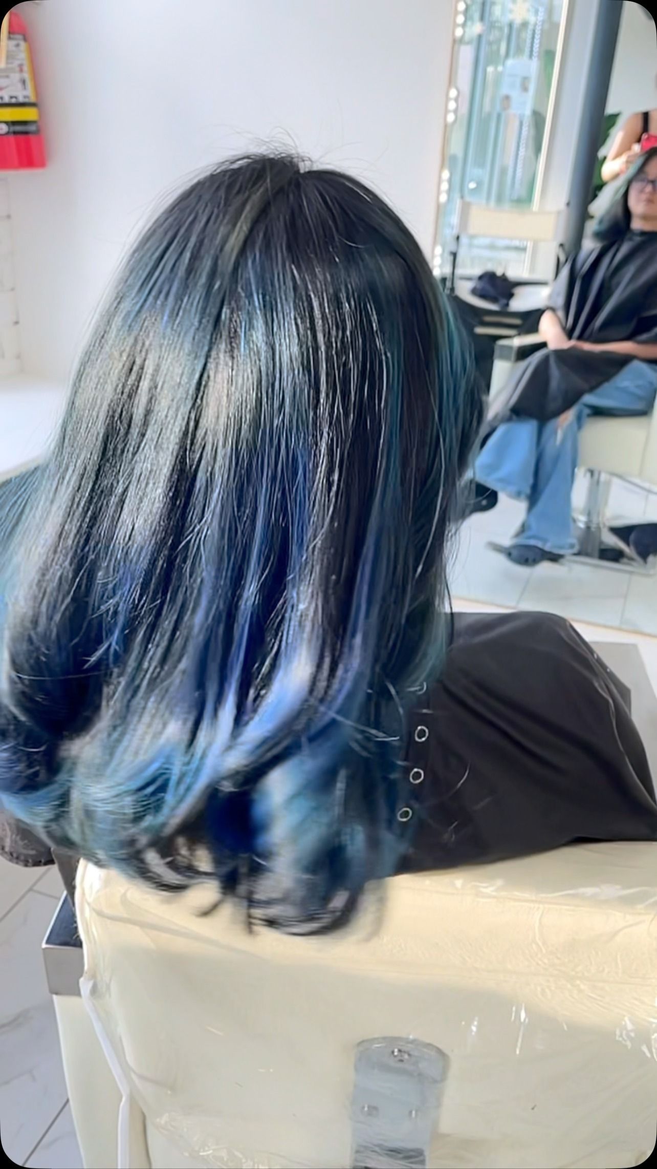 A woman with blue hair is getting her hair dyed in a salon.