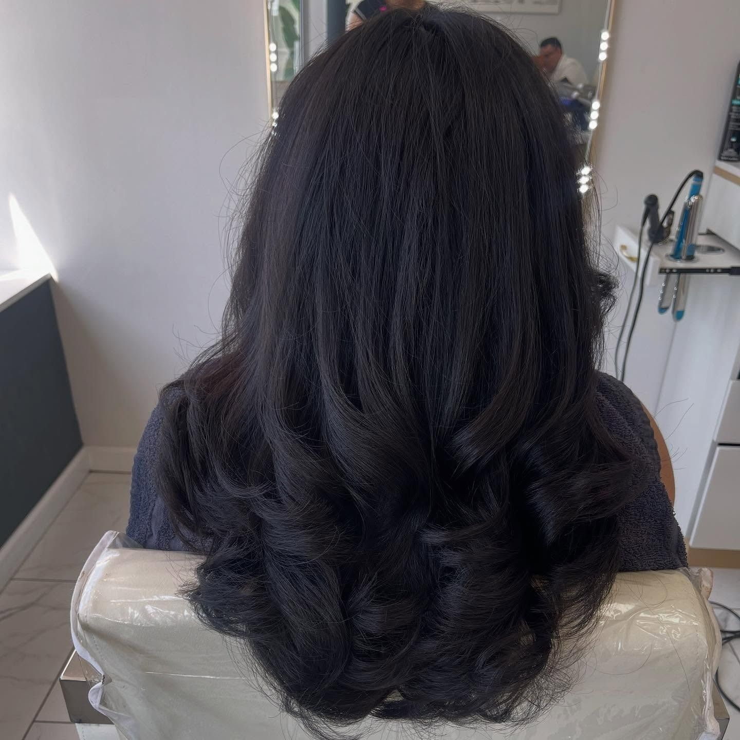 A woman with long black hair is sitting in a chair in front of a mirror.