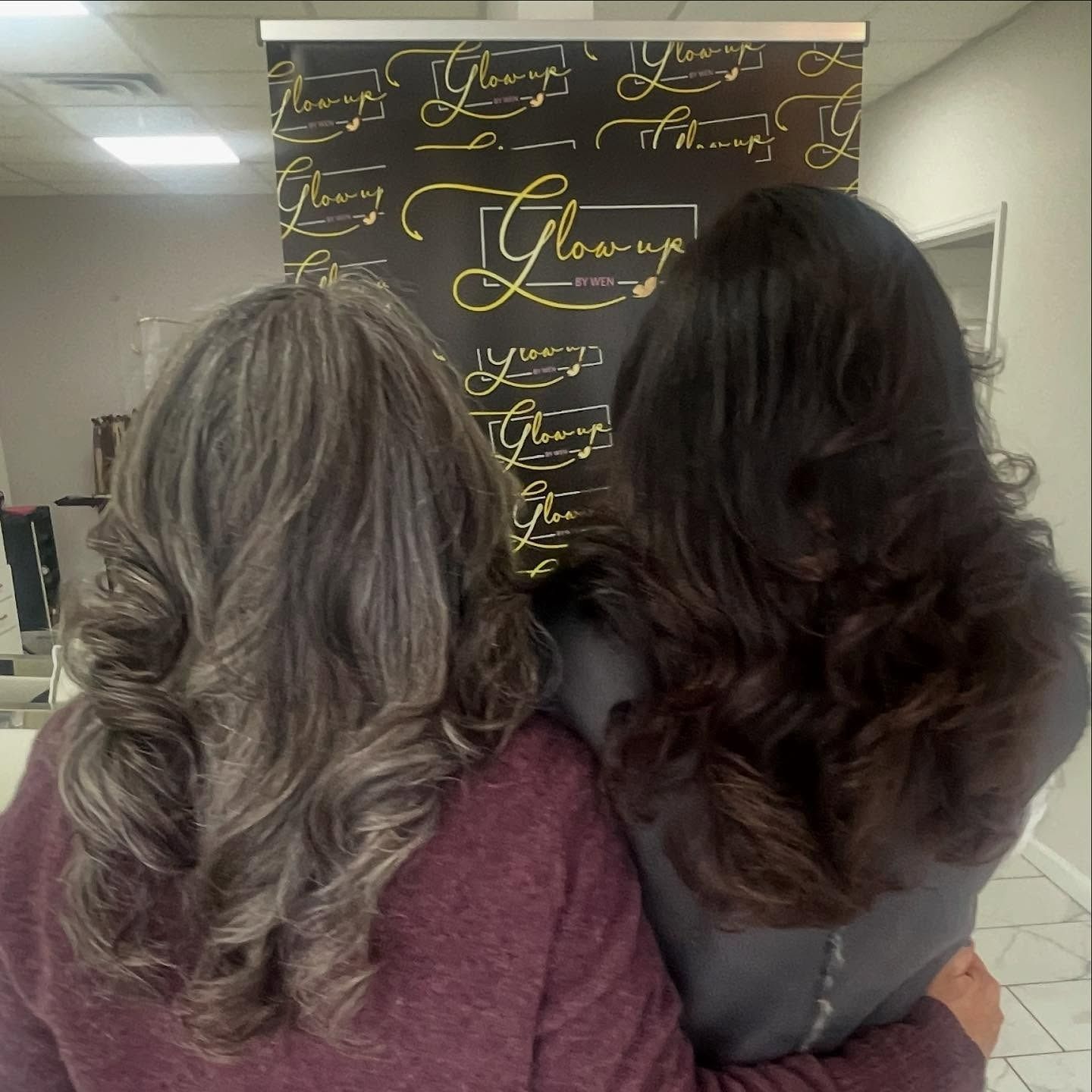 Two women are hugging each other in front of a sign that says glowing