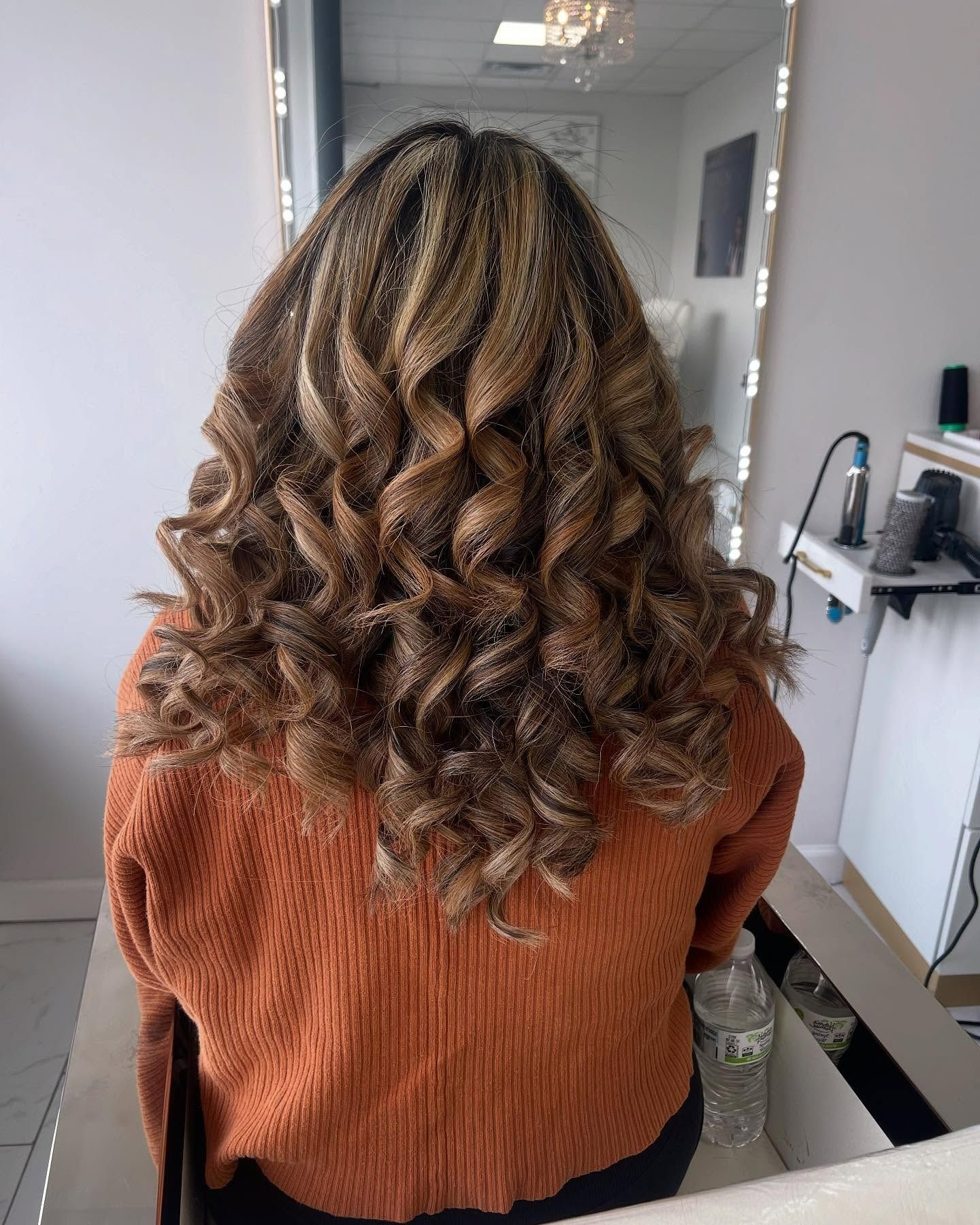 A woman with curly hair is sitting in front of a mirror.