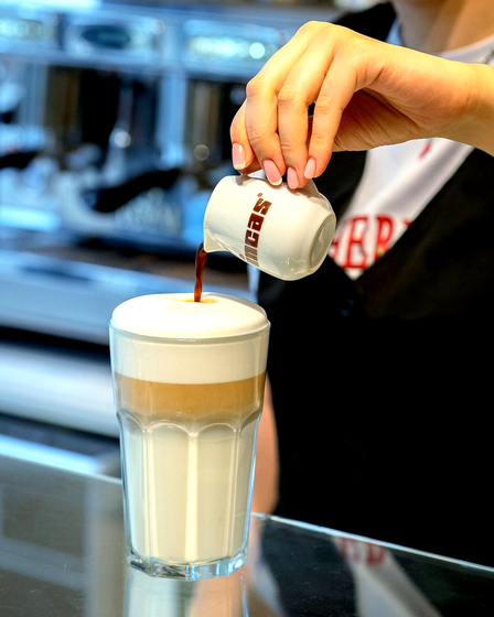 Barista pouring coffee into a layered latte in a clear glass.Domenica 
Home made italian pastries, food & coffee 
