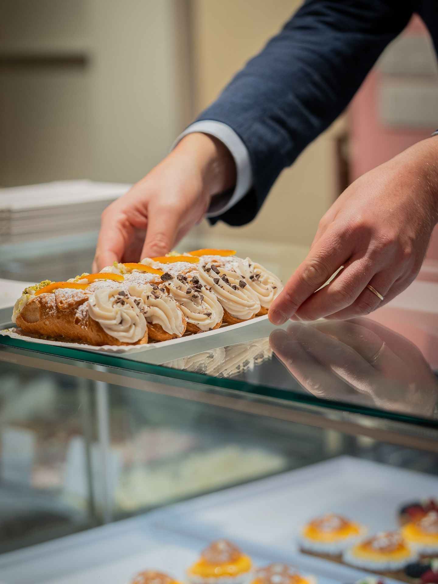 Person placing a cream-topped pastry on a display shelf in a bakery.
