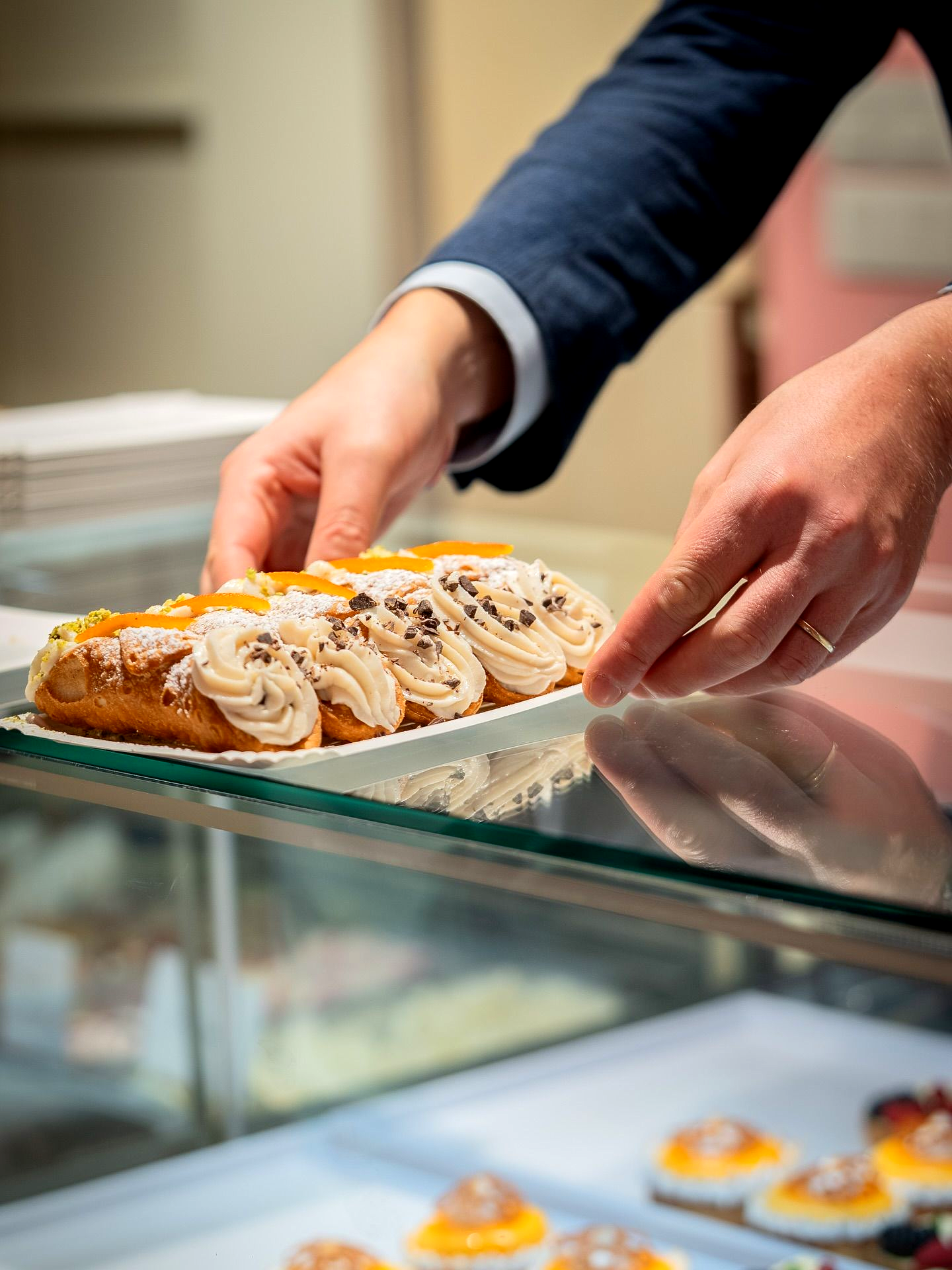 Hands placing a pastry, topped with cream and fruit, on a shelf inside a glass display case.Domenica
Home made italian pastries, food & coffee
