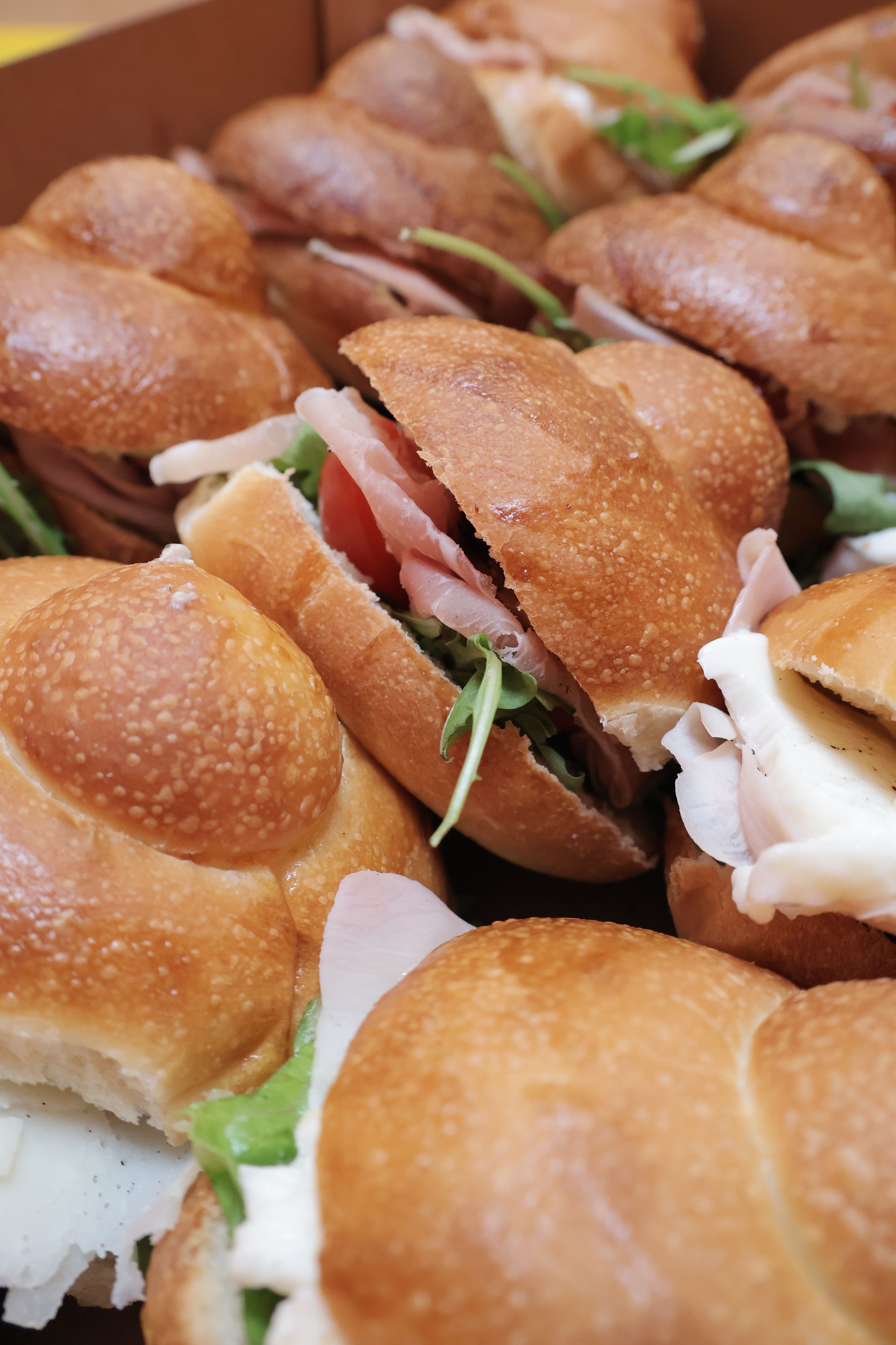 Close-up of a box of mini sandwiches on rolls, filled with meat, tomato, and arugula.Domenica 
Home made italian pastries, food & coffee 
