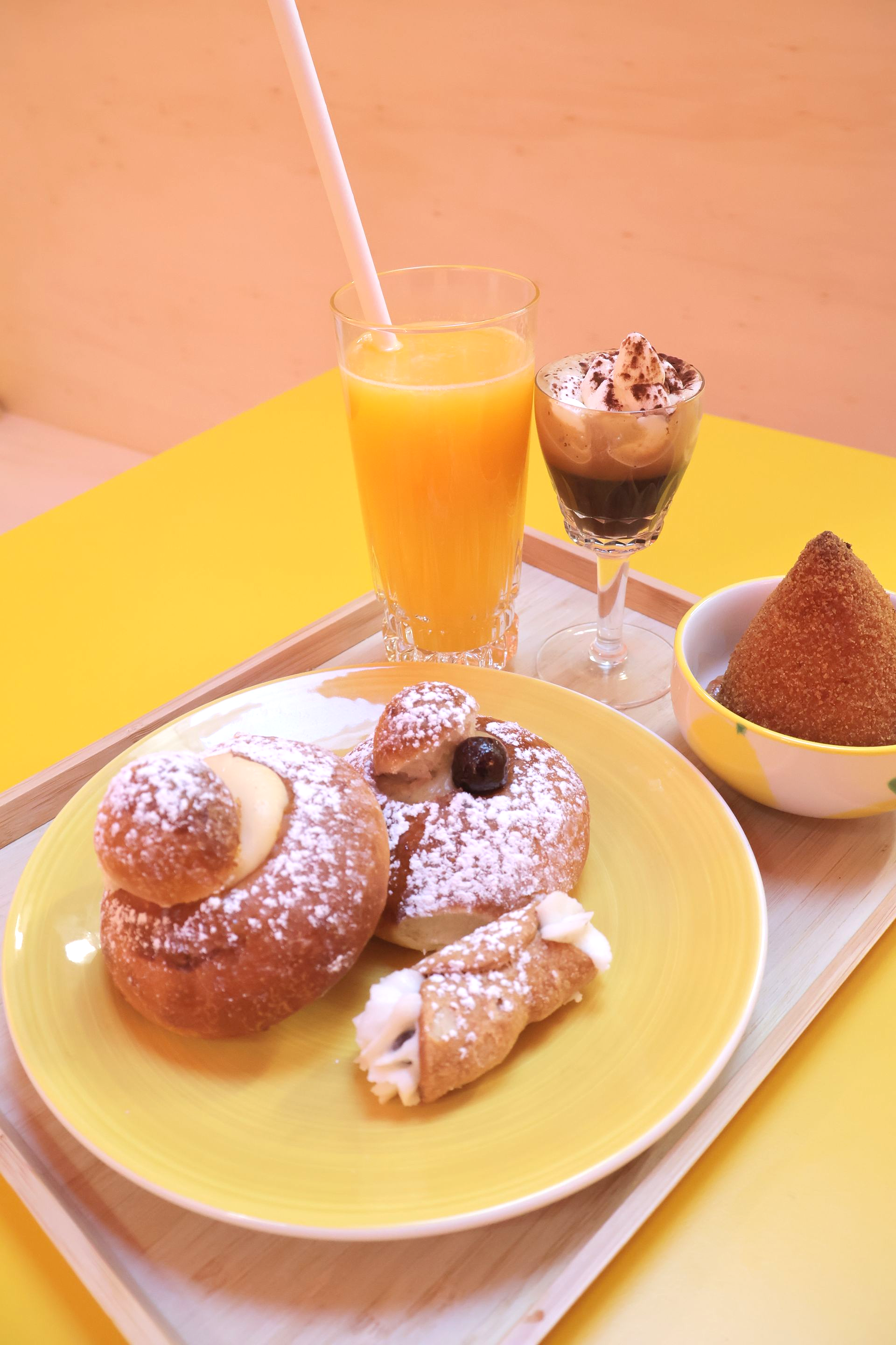 Yellow plate with pastries, orange juice, coffee, and a cone-shaped fried snack, on a tray.