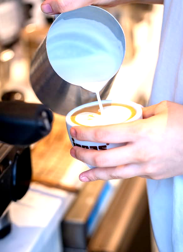 Barista pouring steamed milk into coffee, creating a heart-shaped design.