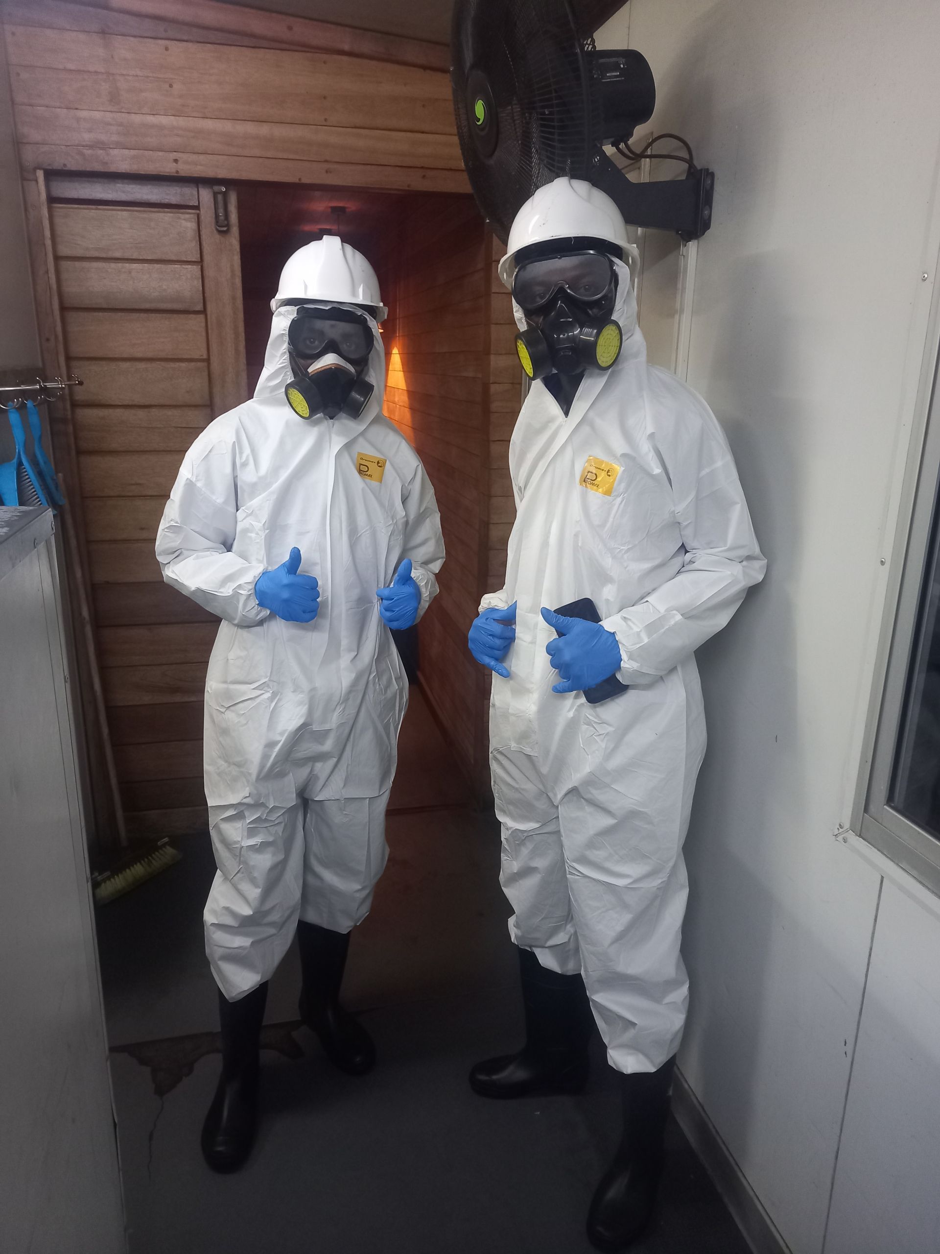 Two people in white hazmat suits, thumbs up, inside a building.
