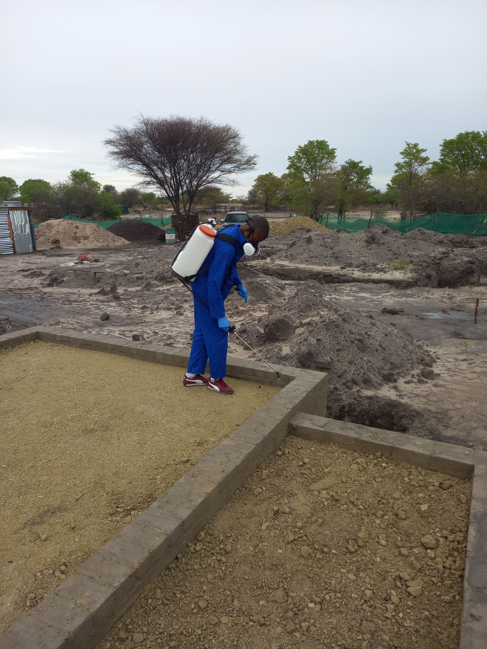 Person in blue protective suit spraying a gravel surface outdoors.