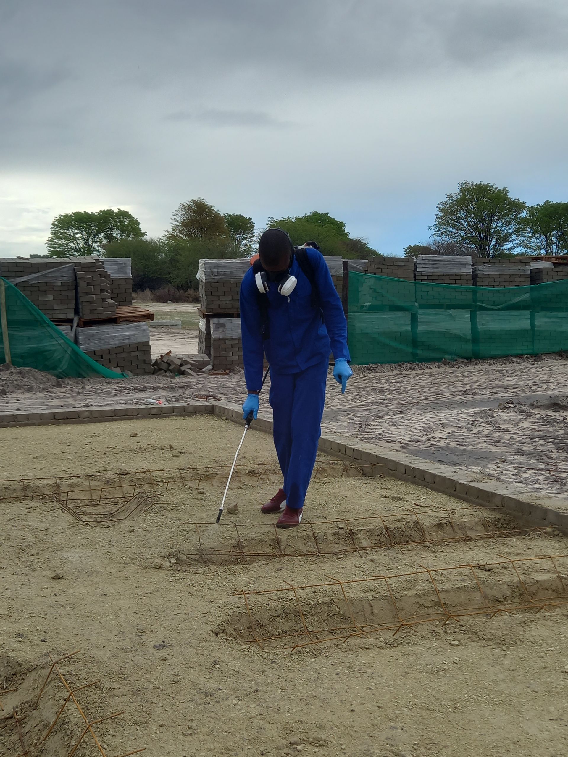 Person in blue protective suit surveying gravel with a measuring tool outdoors.