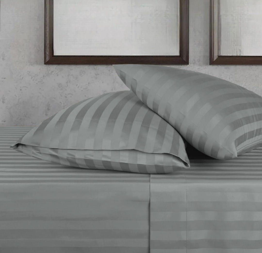 Ropa de cama de rayas beige con dos almohadas sobre una cama, contra una pared gris con marcos de fotos.