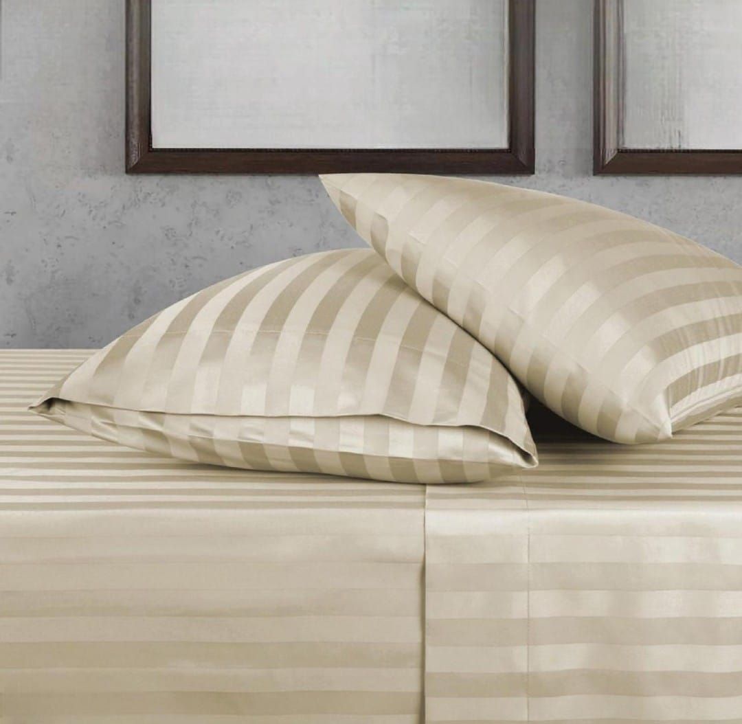 Ropa de cama de rayas beige con dos almohadas sobre una cama, contra una pared gris con marcos de fotos.