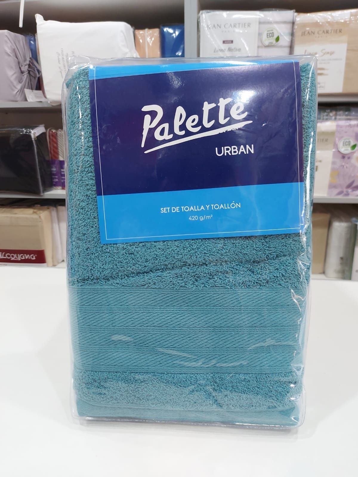 Juego de toallas de color gris oscuro envuelto en plástico con etiqueta azul y blanca.