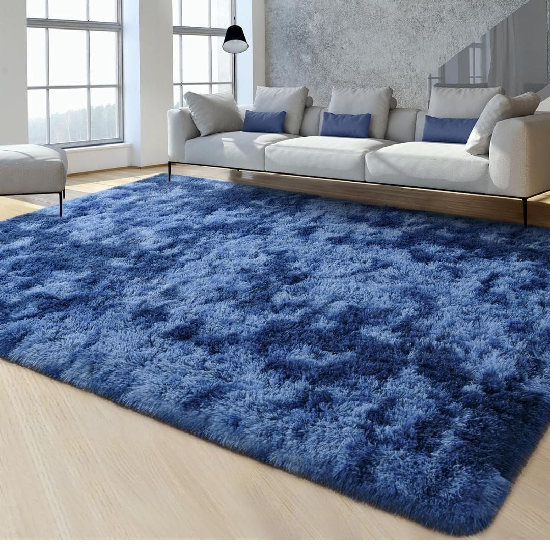 Alfombra peluda morada en una sala de estar con sofá, sillón y mesa de centro. Hay un libro sobre la alfombra.