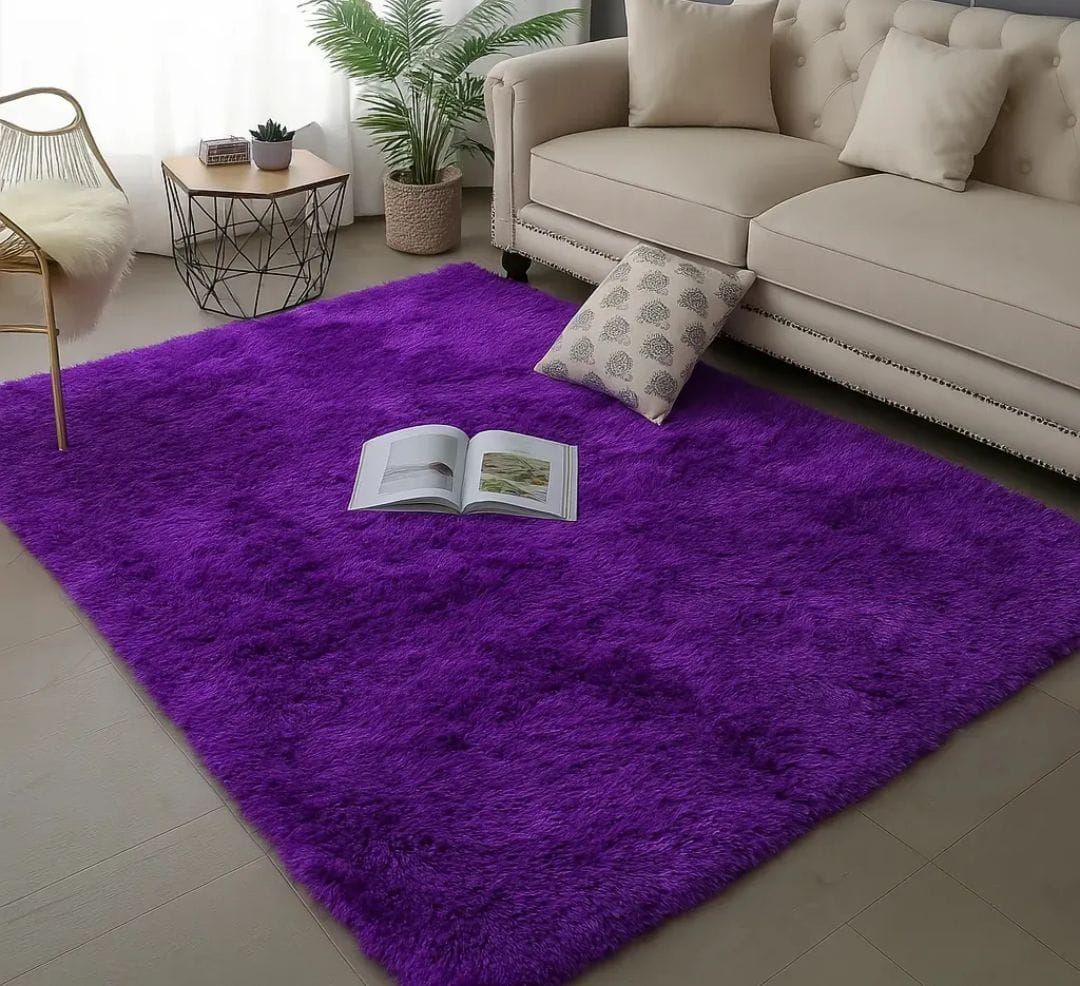 Alfombra peluda morada en una sala de estar con sofá, sillón y mesa de centro. Hay un libro sobre la alfombra.