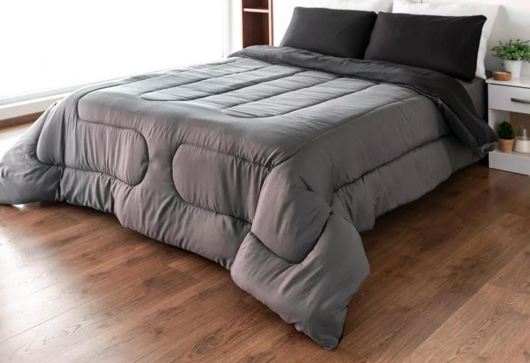 Un edredón y almohadas de color negro sobre una cama en una habitación con pisos de madera.