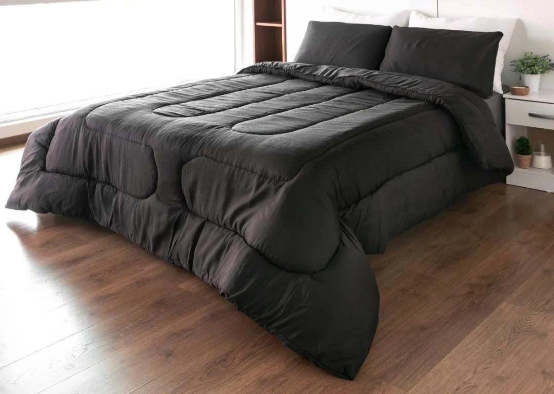 Un edredón y almohadas de color negro sobre una cama en una habitación con pisos de madera.