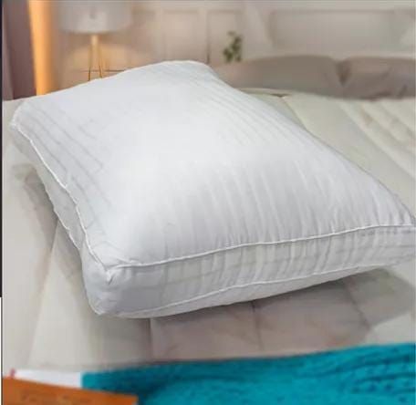 Dos almohadas blancas apiladas, contra una pared de piedra, con bambú y pequeñas rocas.