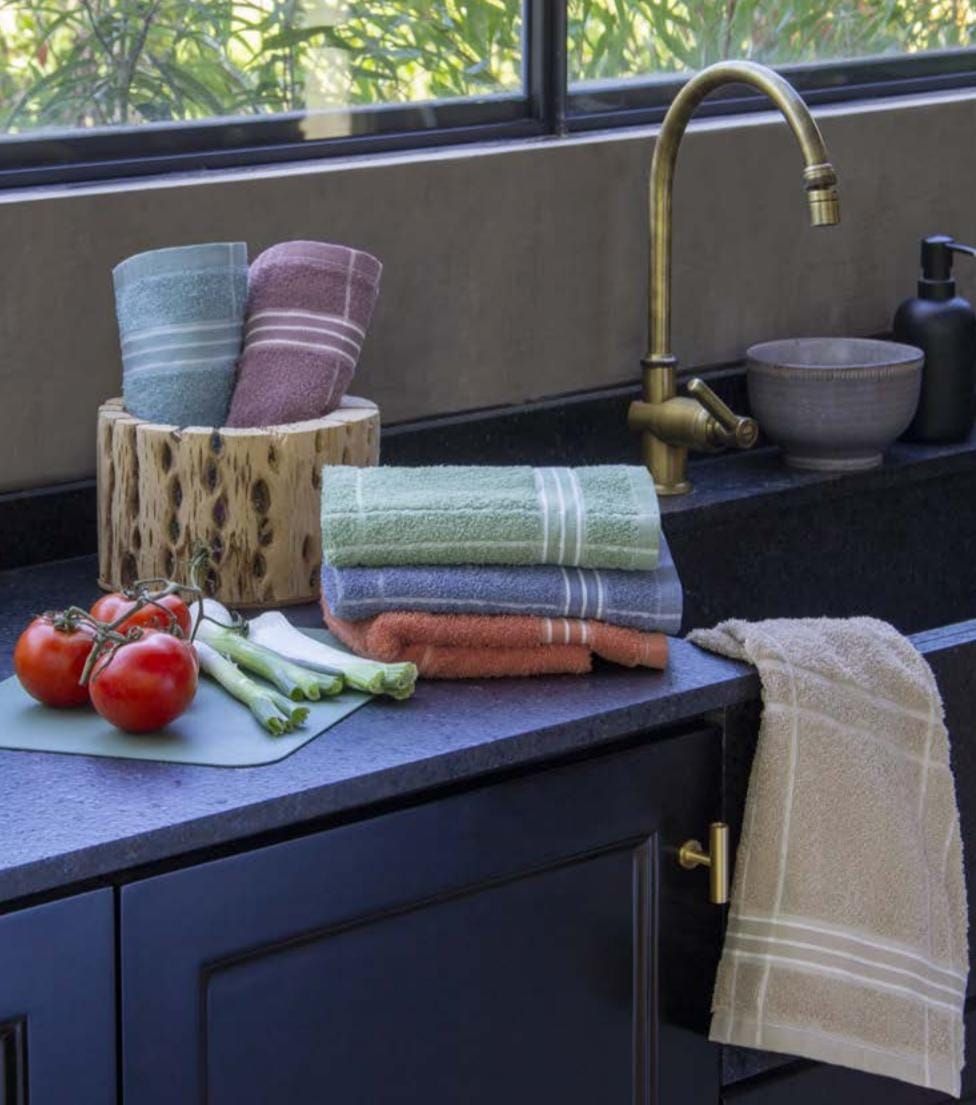Escena de cocina con toallas, tomates, grifo y fregadero. Toallas de diferentes colores apiladas y colgadas.