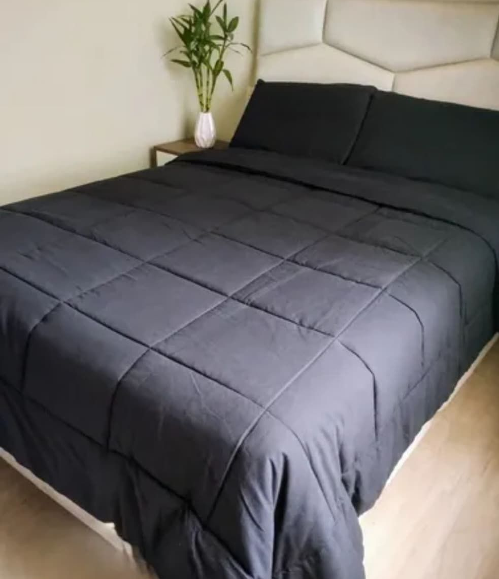 Edredón y almohadas negras sobre una cama en un dormitorio, con una planta en una mesita de noche.