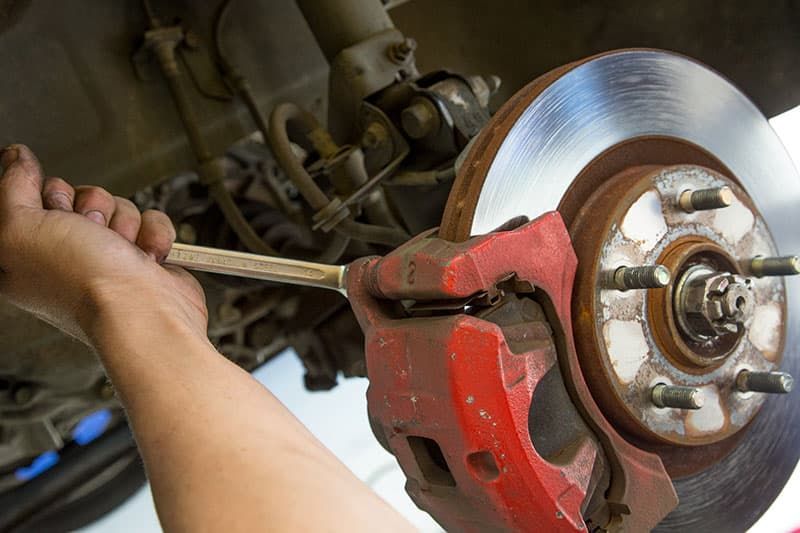 A Person Is Fixing a Car Brake with A Wrench — Marsh Mechanics and Auto Electrical in Maddingley, VIC