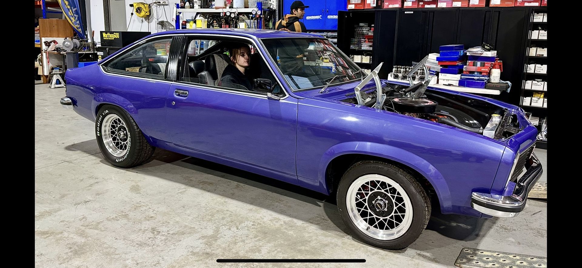A Woman Sitting In The Front Seat Of A Purple Car In A Shed — Marsh Mechanics and Auto Electrical in Maddingley, VIC