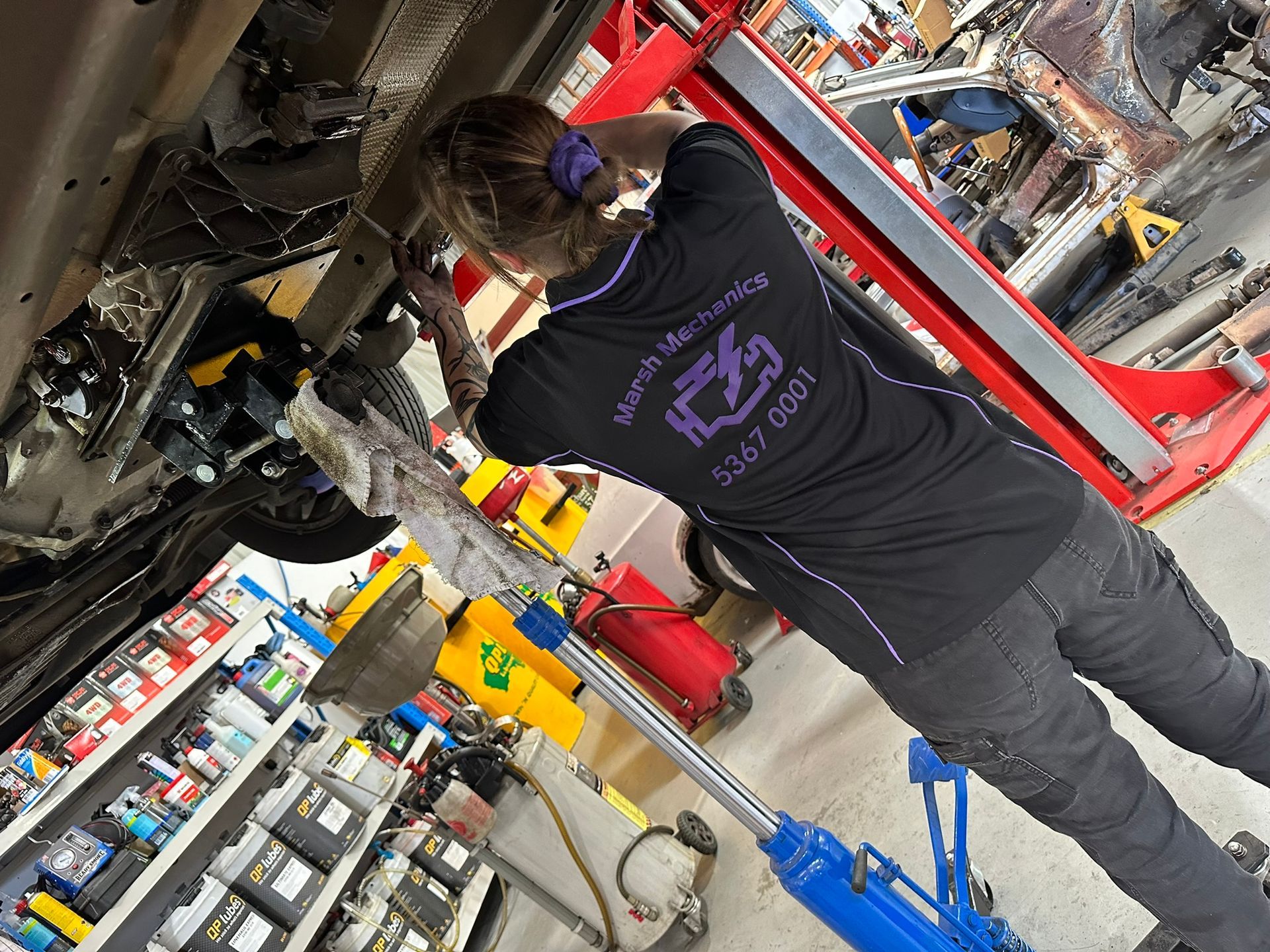 A Woman Working Underneath A Hoisted Car — Marsh Mechanics and Auto Electrical in Maddingley, VIC