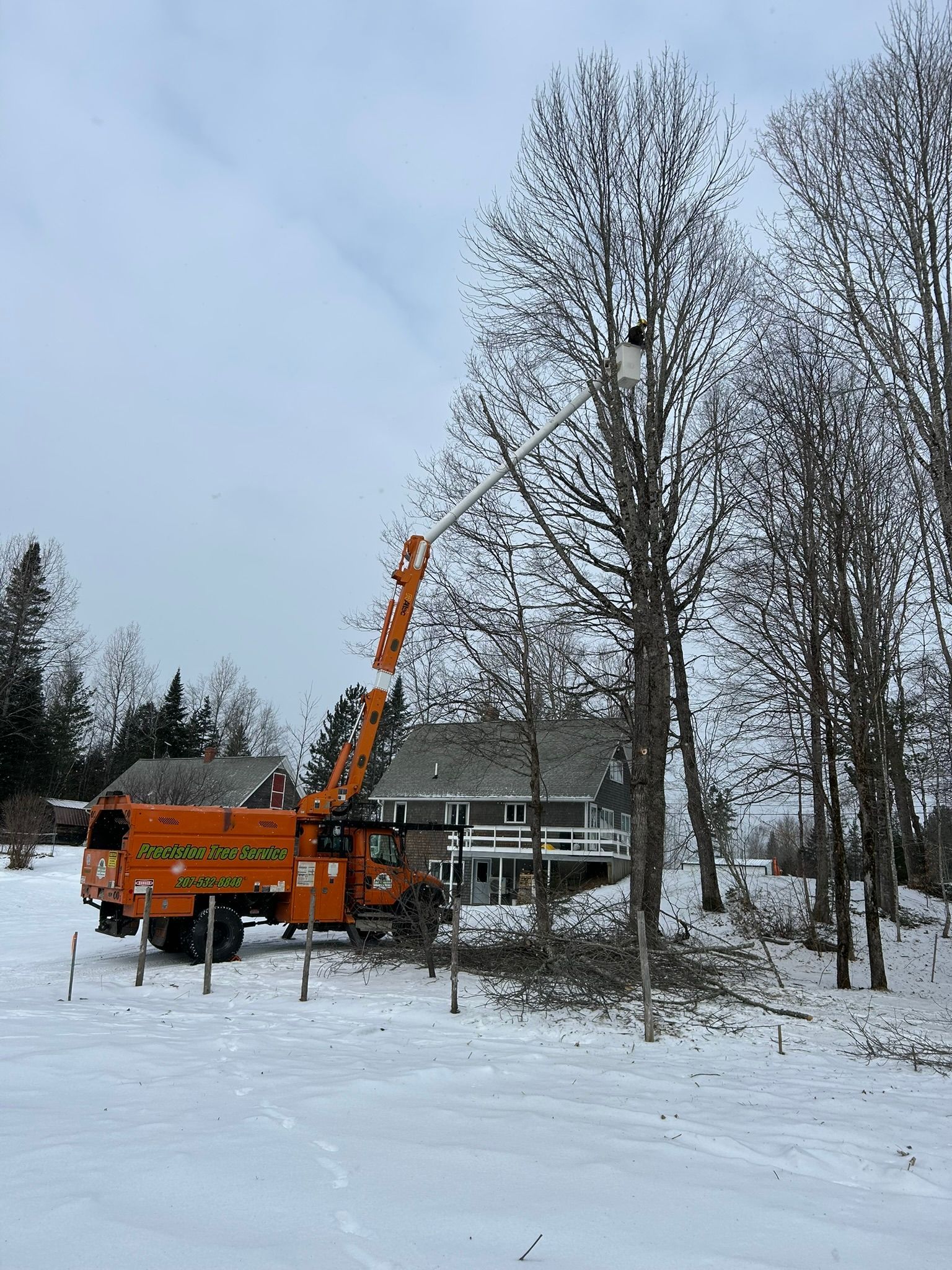 An orange truck is parked in the snow in front of a house.
