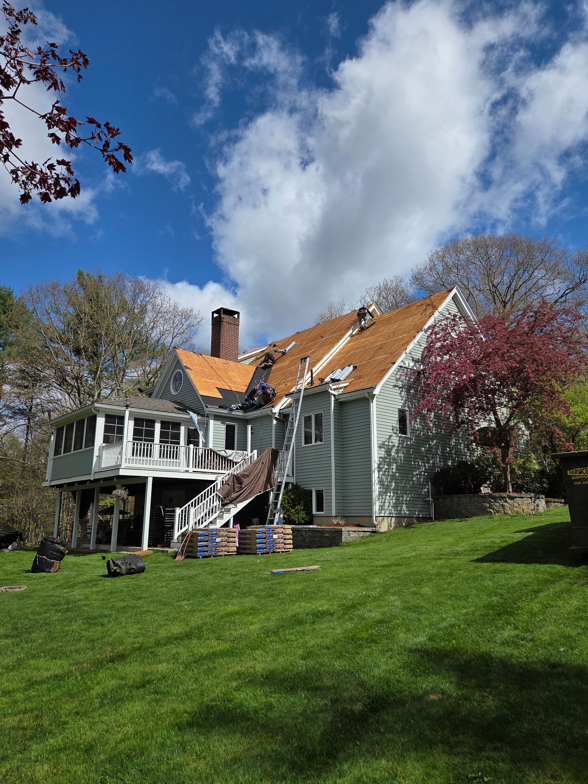 Green house with a white porch and orange roof under a blue sky, viewed from a grassy lawn
